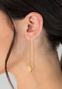 Orecchini a goccia in oro con un ciondolo rotondo texturizzato e una catena sottile. Il design è minimalista, mettendo in risalto il dettaglio circolare e la finitura liscia.