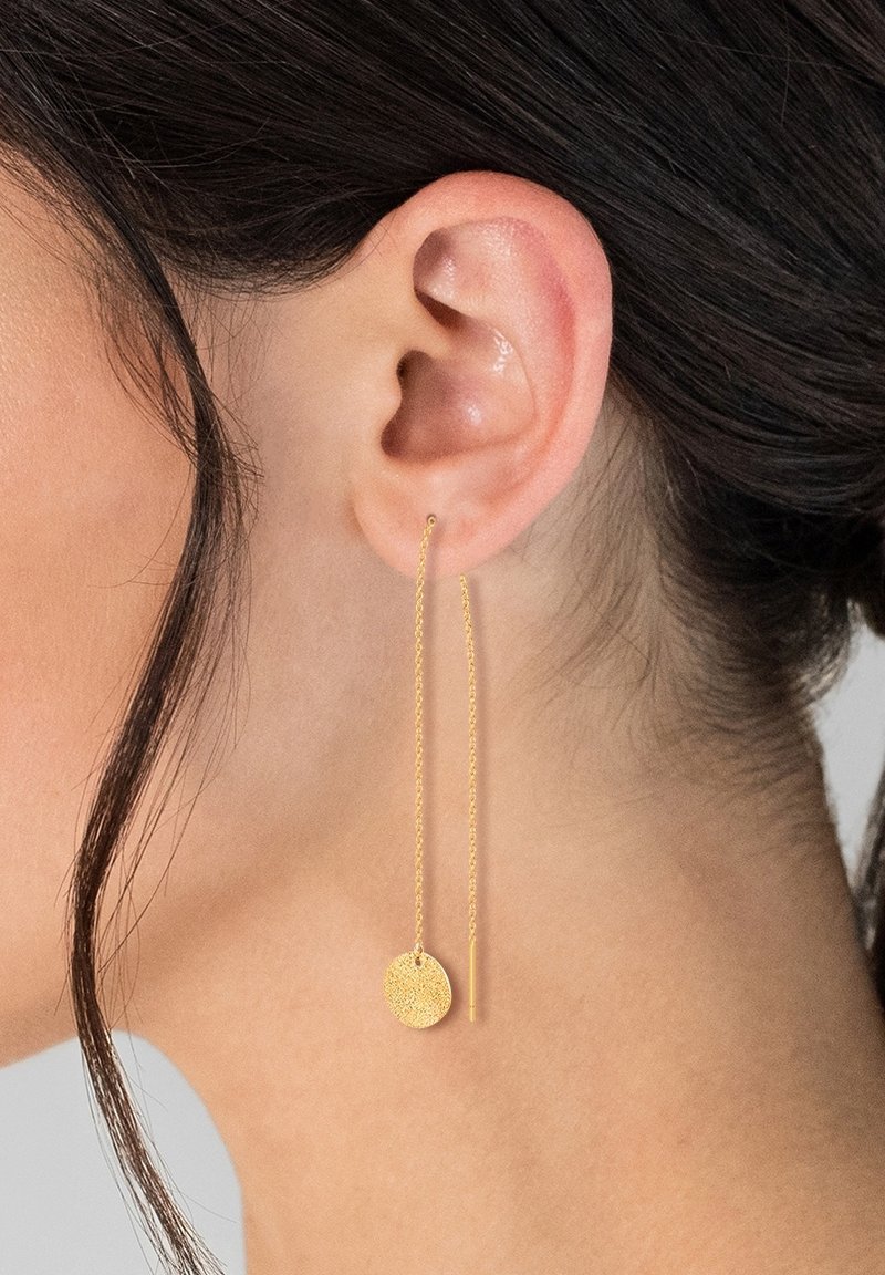 Orecchini a goccia in oro con un ciondolo rotondo texturizzato e una catena sottile. Il design è minimalista, mettendo in risalto il dettaglio circolare e la finitura liscia.