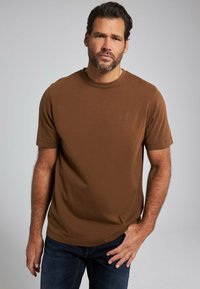 Camiseta de tirantes cortos marrón, hecha de una tela suave, con cuello redondo; presenta un sutil logotipo en relieve en la parte superior izquierda.