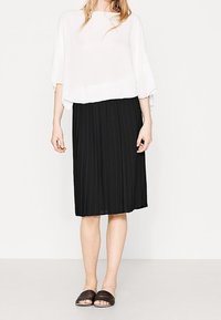 Top bianco a maniche corte, leggero e morbido, abbinato a una gonna midi nera plissettata e sandali neri a scivolo. Tessuto liscio con un design fluido.