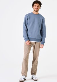 Sudadera azul claro con cuello redondo, puños acanalados y un sutil detalle de logo. Combinada con pantalones de pana beige y sneakers blancos.