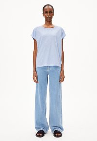 Gestreepte lichtblauwe t-shirt met korte mouwen, gecombineerd met losse lichtblauwe jeans en zwarte sandalen. Effen achtergrond.