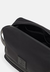 Svart nylonresväska med en slät yta, dragkedjeslutning och logopatch. Har en rymlig, ofodrad insida med en öppen design.