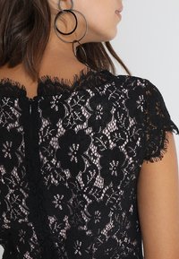 Svart spetsklänning med blommönster, scalloped halsringning och cap sleeves. Mjuk textur med en dold dragkedja på baksidan.