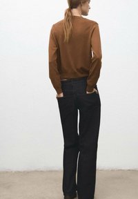 Suéter de punto marrón y pantalones vaqueros oscuros de campana. Los pantalones tienen bolsillos traseros; el suéter tiene puños y dobladillo acanalados.