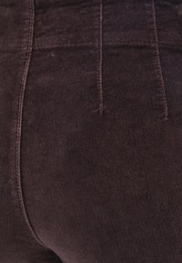 Ciemnofioletowe spodnie z wysokim stanem, wykonane z miękkiego, teksturowanego materiału. Posiadają widoczne szwy, dwie tylne kieszenie i gładkie wykończenie.