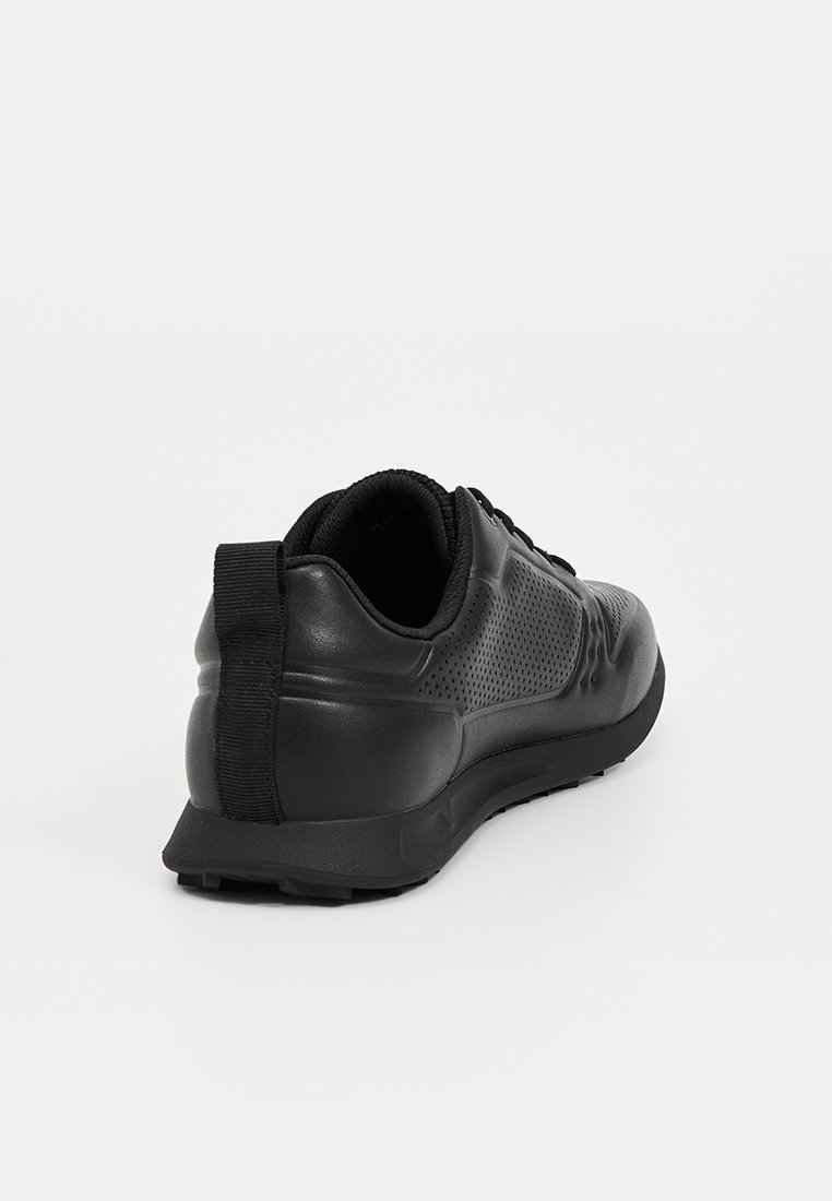 Chaussure de sport noire en matériau synthétique lisse, avec un panneau arrière texturé, une semelle en caoutchouc et une languette pour un enfilage facile.