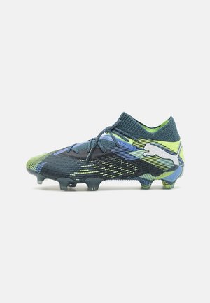 Chaussure de football bleu foncé et vert néon avec lacets, tige texturée et semelle à crampons, avec un logo Puma blanc sur le côté.