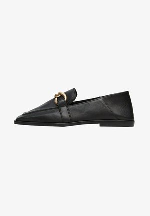 Chaussures noires en cuir à enfiler avec un bout pointu et un design angulaire. Elles possèdent un accent en métal doré sur le dessus et une semelle plate.