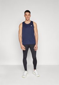 Navy blue sleeveless athletic top, black fitted leggings, and white sports shoes with green accents, worn by a male model.