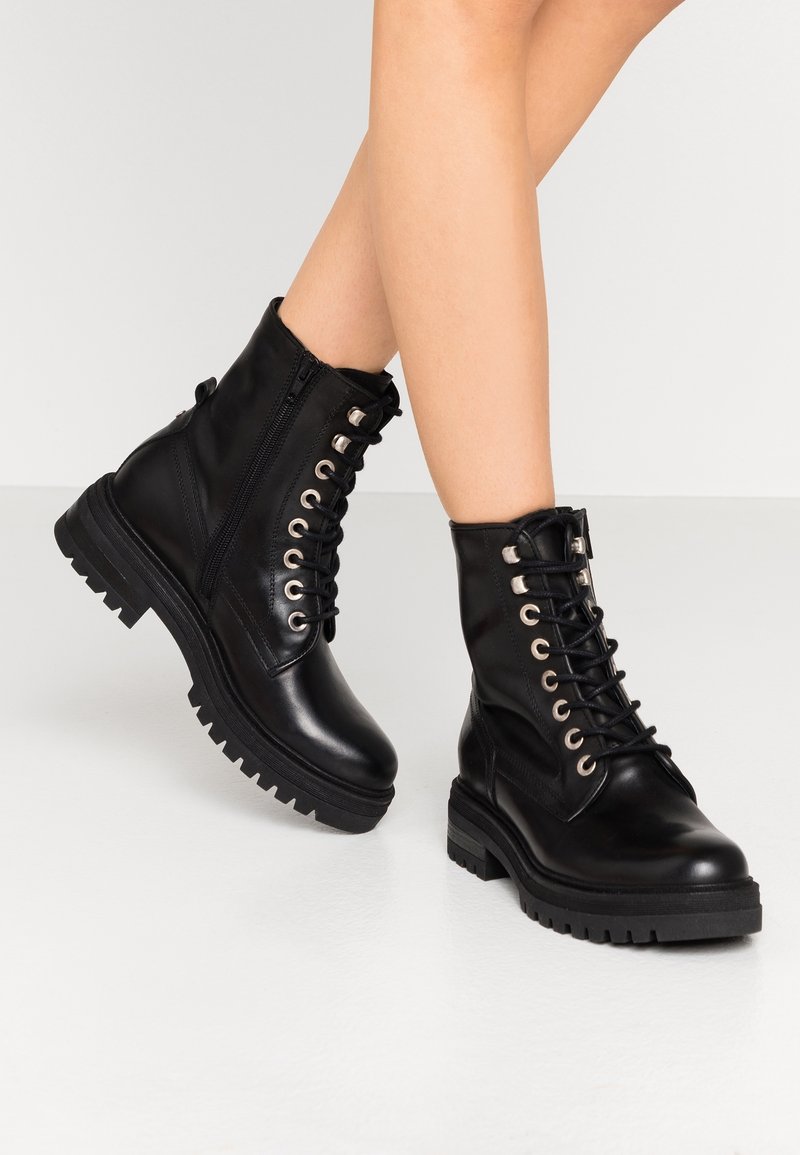 Bottines en cuir noir avec un laçage sur le devant, une semelle épaisse et une fermeture éclair intérieure. Œillets métalliques et finition texturée ajoutent des détails.