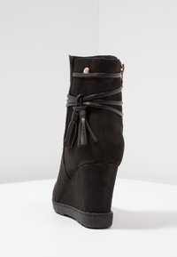 Stivaletto alla caviglia nero con finitura in suede liscia, caratterizzato da un accento legato e dettaglio della cerniera metallica. Tacco testurizzato e suola in gomma nera.