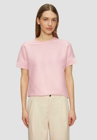 Gestreiftes, kurzärmliges Oberteil in hellrosa und weiß, mit rundem Halsausschnitt und lockerer Passform, kombiniert mit beigen Hosen.