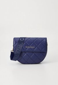 Kék tengerészkék steppelt bőr keresztpántos táska lekerekített formával, aranyszínű fémrészletekkel és logónyomott pánttal. A fedelén sima kivitelű záródás található.