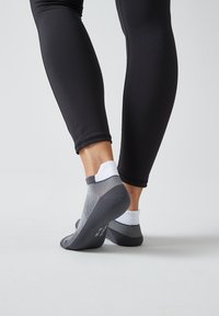Grau und weiße Knöchelsocken mit strukturiertem Grip und verstärkter Ferse, kombiniert mit eng anliegenden schwarzen Leggings, die eine Nahaufnahme des Unterschenkels zeigen.