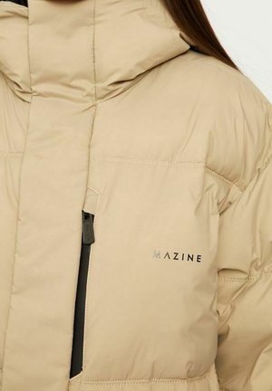 Beige pufferjakke med høj krave, med en lynlåslomme på brystet, quiltdetaljer og et sort logo på fronten.