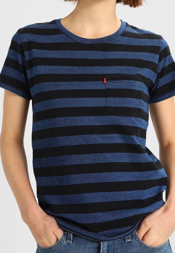 Personne portant un t-shirt à rayures horizontales bleu marine et noir à manches courtes avec une poche sur la poitrine, les mains dans les poches d'un jean bleu.