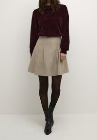 Maglione borgogna a trama con un collo alto abbinato a una gonna plissettata a scacchi beige. Calze nere e stivaletti neri con punta.