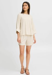 Ensemble blouse et short en lin dans une teinte beige clair. La blouse présente un col bateau et des manches larges ; le short est doté d'une taille élastique.