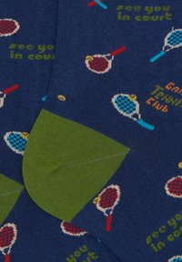 Calze blu con motivi di racchette da tennis e testo in verde e giallo, con una sezione solidale in verde per il tallone e la punta. Texture a maglia tipo maglione.