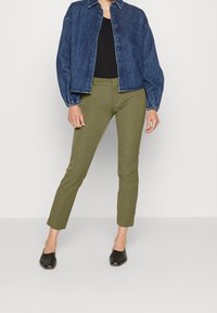 Jeansjacka i mörkblått med avslappnad passform, svart topp under, olivgröna byxor med slim fit, och svarta slip-on skor.