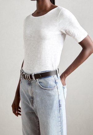 Bílé, krátké rukávy, přiléhavé tričko z lehké látky, doplněné o vysoké světlé džíny s opaskem tmavě hnědé barvy.