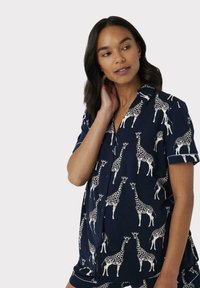 Conjunto de pijama de manga corta en color navy con un estampado de jirafas en color crema. La camiseta tiene cuello y botones; los pantalones cortos tienen un diseño a juego.