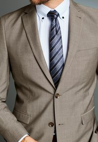 Blazer marrón claro con una textura sutil, con cierre de un solo botón y solapas con muesca. Combinado con una camisa de vestir a rayas y una corbata oscura a rayas.