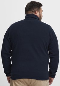 Pullover in pile blu navy con collare alto, caratterizzato da una texture morbida e maniche lunghe, visto da dietro, che evidenzia una finitura liscia.