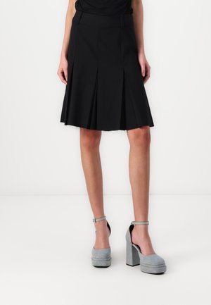Black pleated skirt with a waistband. Paired with grey high-heeled shoes, featuring a textured finish and ankle straps.