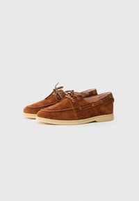 Brown suede boat shoes with a round toe, lace-up design, and metal eyelets. Features a tan rubber sole for traction and comfort.