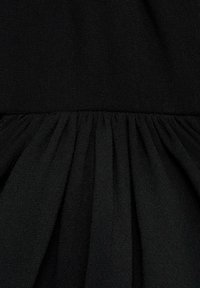 Prenda negra con tela suave y texturizada, con detalles fruncidos en la cintura que crean un efecto fluido y en capas.