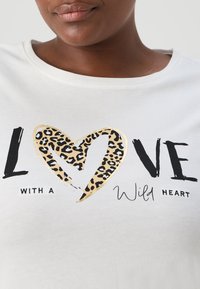 Bílý tričko s krátkým rukávem, na kterém je černým písmem nápis "LOVE". Ve středu je zvýrazněné srdce ve zlaté barvě s leopardím potiskem.