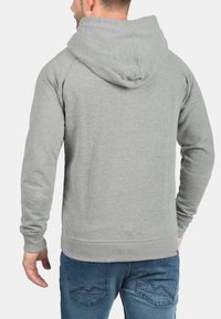 Gray hooded sweatshirt with textured fabric, a kangaroo pocket, and ribbed cuffs. Worn with blue jeans, showing a casual, relaxed fit.