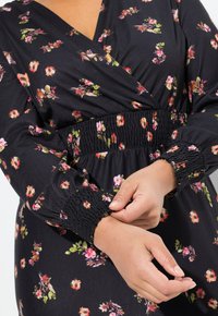 Schwarzes florales Wickelkleid mit langen Ärmeln, gerafften Manschetten und tailliertem Bund. Überzieht farbenfrohe Blumenmuster in Rosa- und Grüntönen.