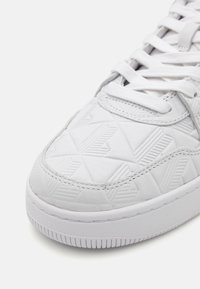 Hvit sneakers med et teksturert geometrisk mønster, syntetisk materiale, rund tå og hvite snørebånd, med gummisåle og sømdetaljer.