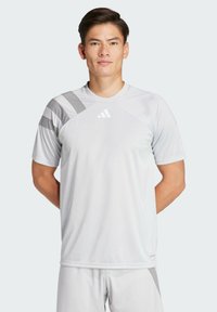 Lichtgrijs sportshirt met korte mouwen, voorzien van een ronde halslijn en diagonale grijze patronen op de schouders. Adidas-logo aan de voorkant.