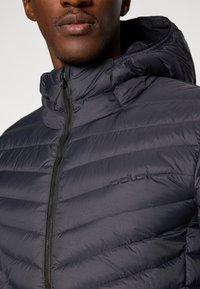 Navy puffer jacket with a zip closure and adjustable hood, featuring horizontal quilted stitching and an embroidered logo in the chest area.