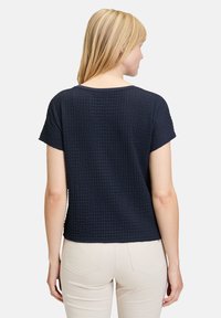 Top corto blu navy con un design a maglia testurizzata. Presenta un collo ampio e un orlo diritto, abbinato a pantaloni chiari.