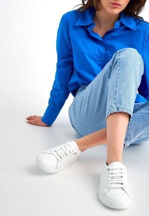 Weiße Sneakers mit einer glatten Lederoberfläche, runder Zehenpartie und dicker Sohle. Mit strukturierten Schnürsenkeln und dezenten Steppnähten.