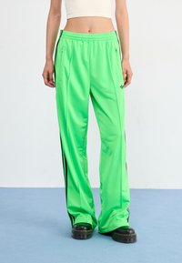 Neon green athletic pants in a relaxed fit, featuring black side stripes, elastic waistband, and zippered pockets for secure storage.
