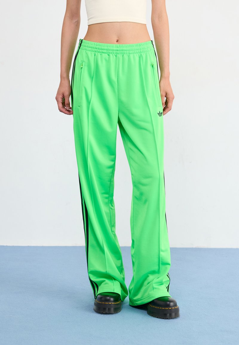 Neon green athletic pants in a relaxed fit, featuring black side stripes, elastic waistband, and zippered pockets for secure storage.