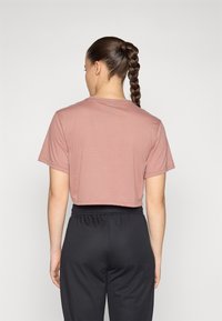 Camiseta de manga corta y recortada en suave tejido malva, con un corte relajado. Combinada con pantalones deportivos negros, que presentan una cinturilla lisa y elástica.