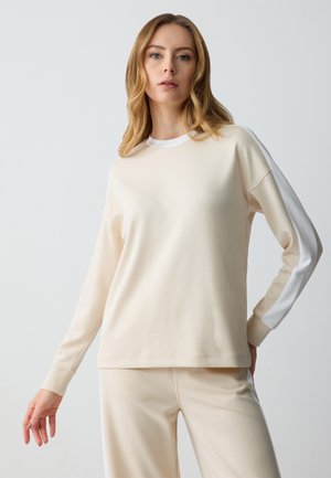 Lichtbeige lange mouw top met een ronde halslijn en witte zijaccenten. Zachte textuur, relaxte pasvorm en ribgebreide manchetten. Gecombineerd met bijpassende broek.