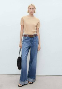 Beige knit short-sleeve top, high-waisted blue wide-leg jeans, brown belt, black woven bag, and black sandals. Simple design and relaxed fit.