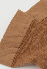 Brunt tyg med spetsdetaljer som visar en slät, något texturerad yta med en vikt kant, som illustrerar en kombination av solida och genomskinliga material.