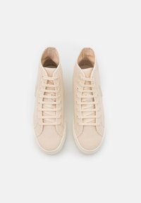 Beżowe sneakersy wysokie wykonane z teksturowanej tkaniny, z okrągłym czubkiem, centralnym sznurowaniem i kontrastującą białą gumową podeszwą.