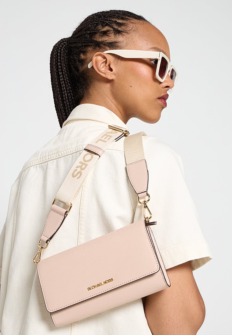 Sac bandoulière en cuir rose avec une finition texturée, quincaillerie dorée et une bandoulière amovible arborant un logo. Poche zippée attachée visible.