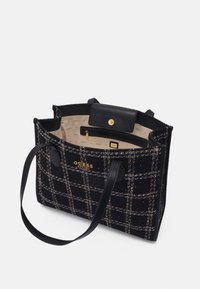 Sac fourre-tout en tweed noir avec un motif à carreaux, logo doré "Guess" et poignées en similicuir noir ; intérieur avec doublure beige et poche zippée.