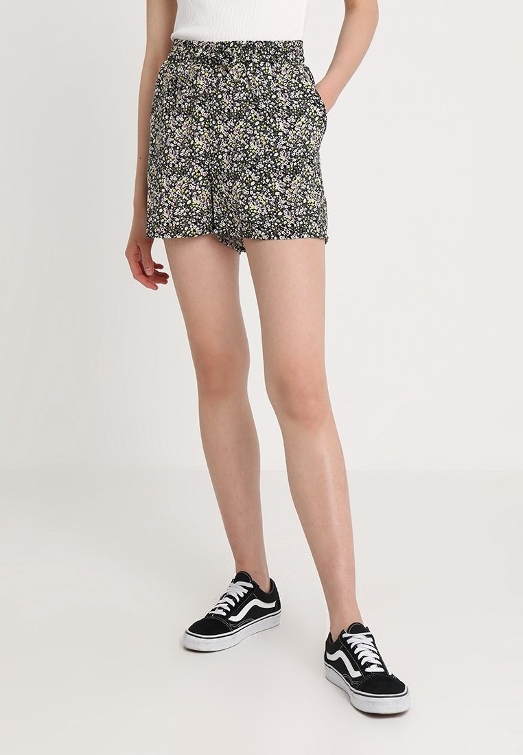 Shorts con stampa floreale su sfondo nero; vita elastica; tasche laterali; tessuto leggero; abbinati a sneakers nere e bianche.